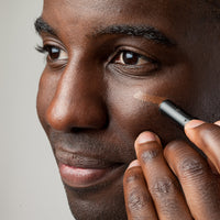 Person applying makeup to their face with a brush on a neutral background